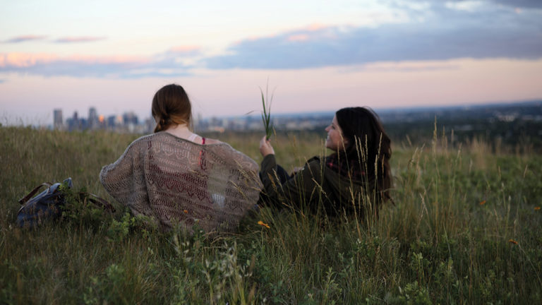 Still from Sweet Night of two characters sitting in a field at sunset.
